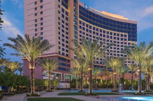 The Wyndham Desert Blue rises against an evening sky behind elegant landscaping dotted with swimming pools and up-lit palm trees