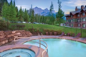 The outdoor pool and hot tub at WorldMark Canmore Banff, a timeshare resort, with the Canadian Rocky Mountains in the distance.